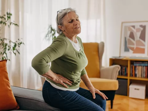 An older woman, sitting at home, holding her side in pain.