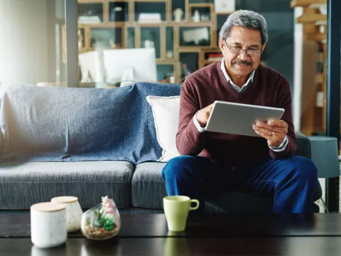 Senior man checking iPad while sitting on a couch while at home.