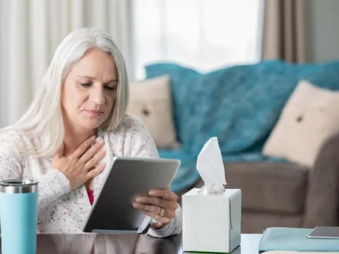 Woman holding heart, looking at tablet