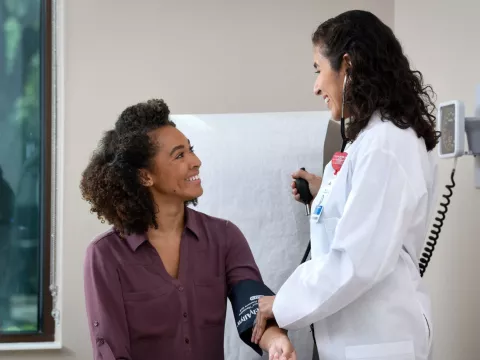 A young woman smiles at her doctor while getting her blood pressure measured.